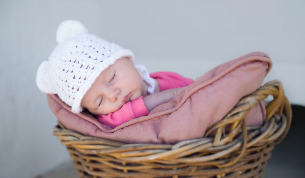 Маленький ребенок в белой шапке спит в корзине