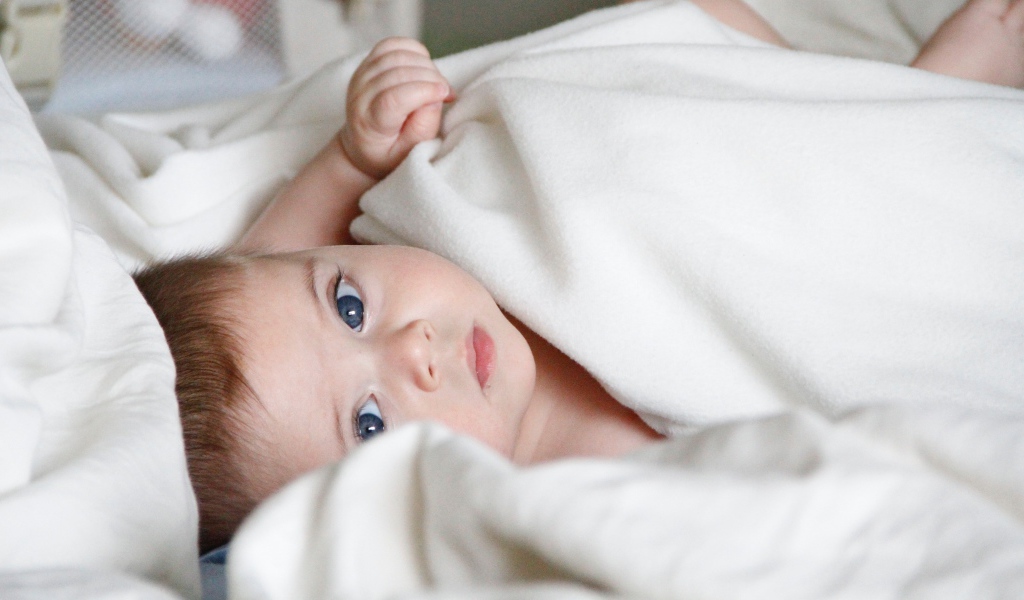 Маленький голубоглазый мальчик под белым покрывалом