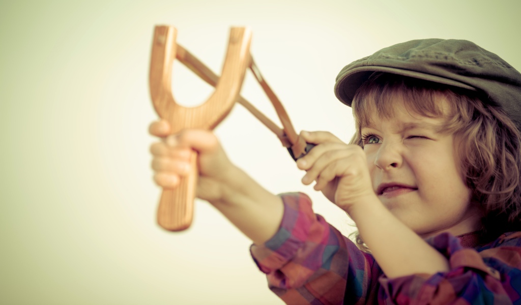 Маленький мальчик в кепке целится с рогатки