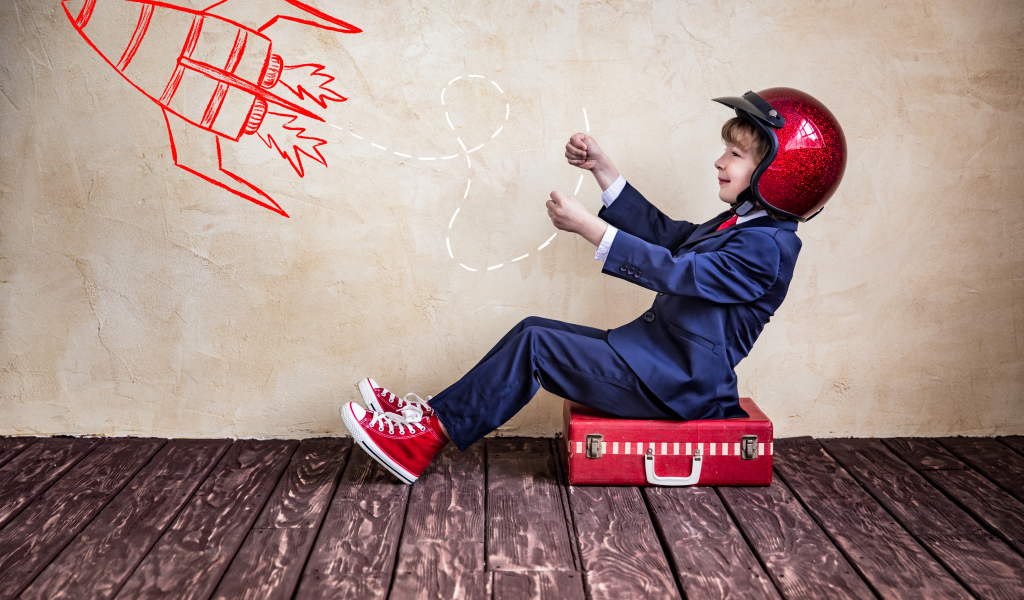 Маленький мальчик в шлеме сидит на чемодане