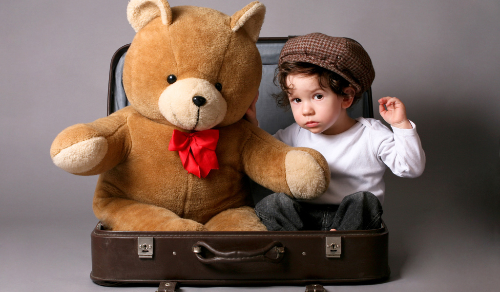 Маленький мальчик сидит в чемодане с плюшевым мишкой 