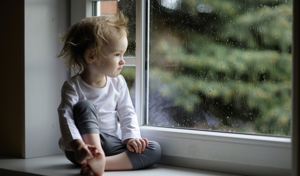 Маленькая девочка сидит на подоконнике у окна