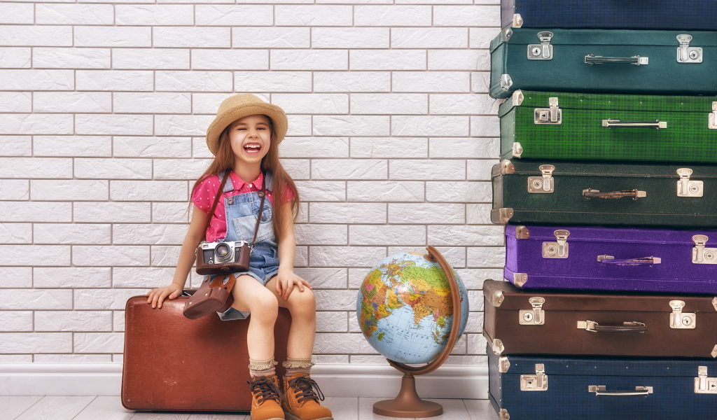 Маленькая девочка с фотоаппаратом сидит на чемодане