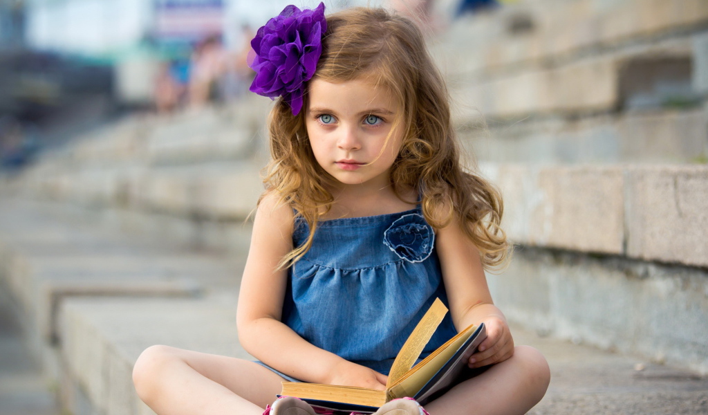 Маленькая девочка с цветком в волосах сидит на ступенях