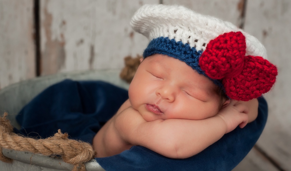 Спящий грудной ребенок в вязаной шапочке с красным бантом