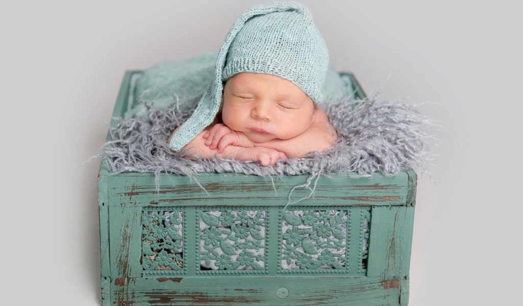 Спящий ребенок в зеленом ящике на сером фоне