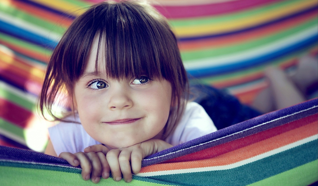 Маленькая кареглазая девочка лежит в гамаке