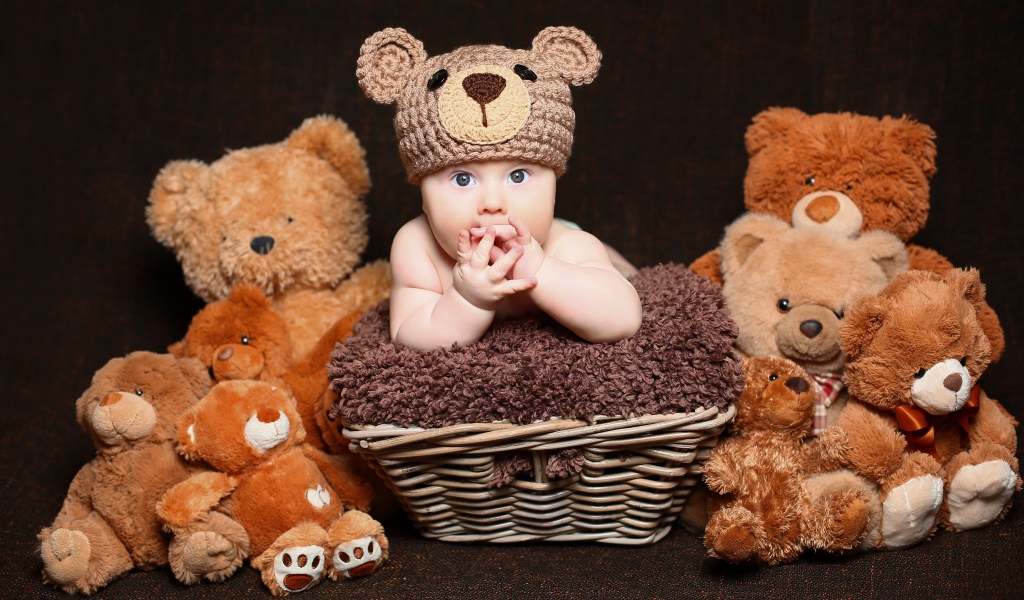 Маленький ребенок в вязанной шапке с  игрушечными медвежатами 