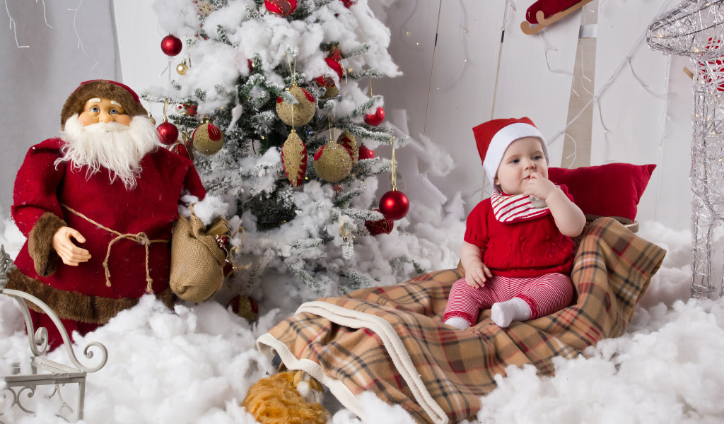 Маленький ребенок в санях у елки с дедом морозом на Новый год 