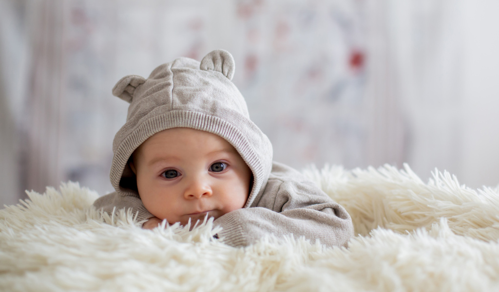 Маленький ребенок лежит на белом меховом покрывале 