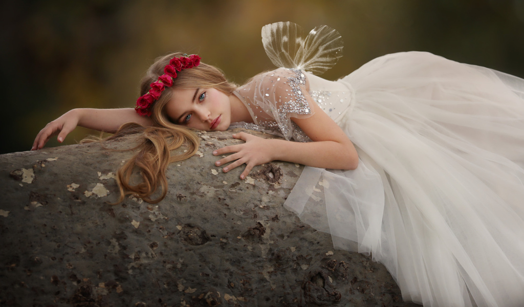 Красивая маленькая девочка в белом платье лежит на камне