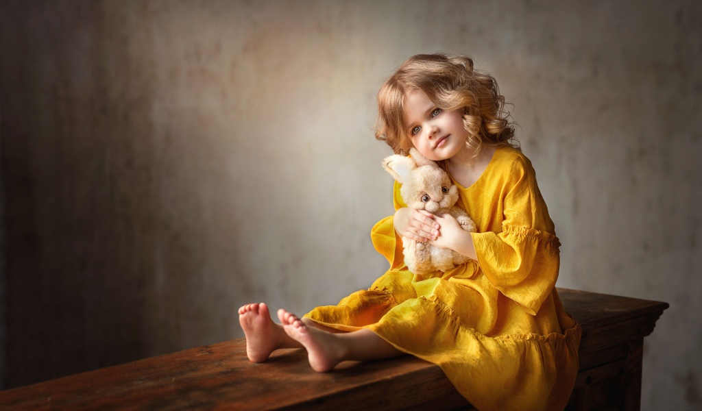 Красивая маленькая девочка в желтом платье с игрушкой