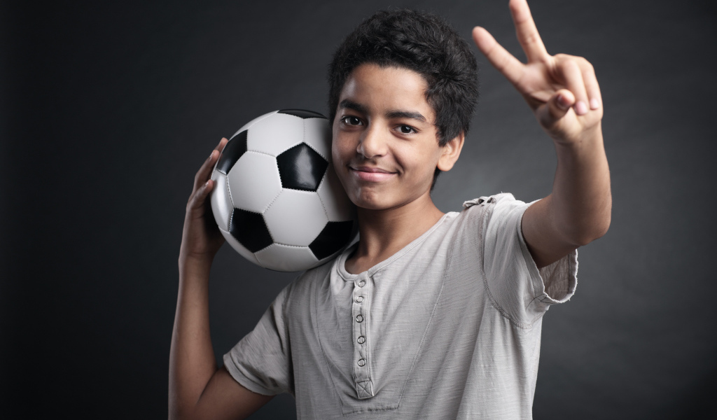 Мальчик с футбольным мячом на плече на сером фоне