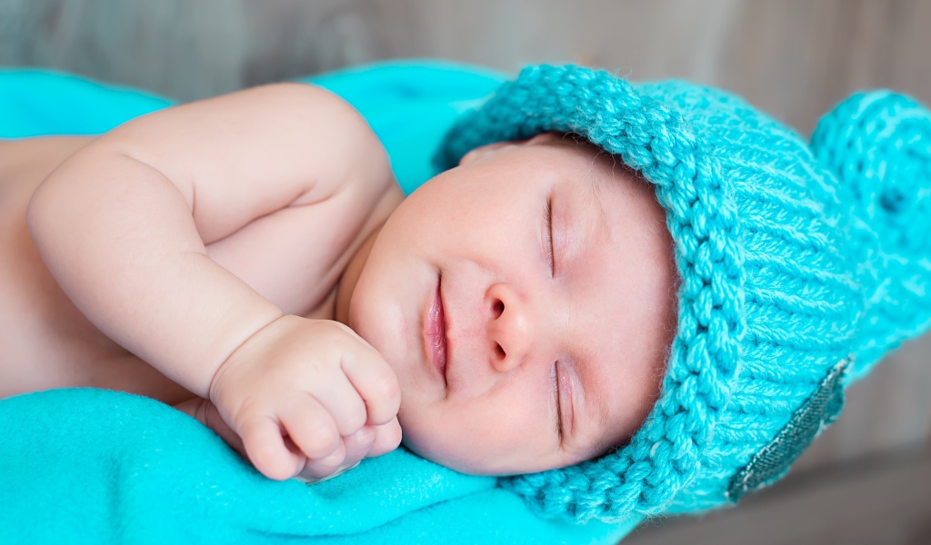 Милый спящий ребенок в голубой вязаной шапке