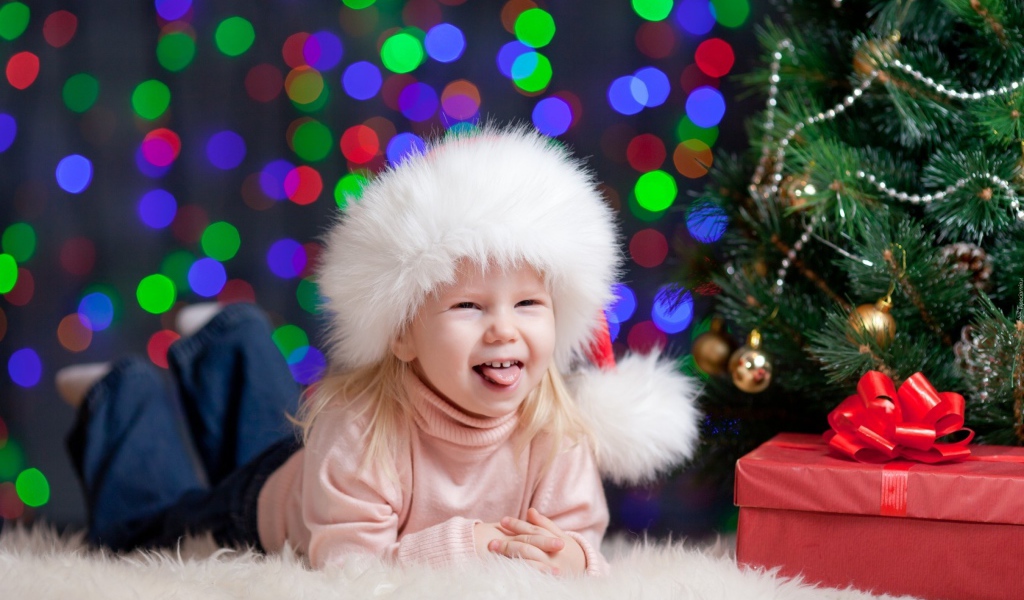 Смешная девочка в новогодней шапке у елки