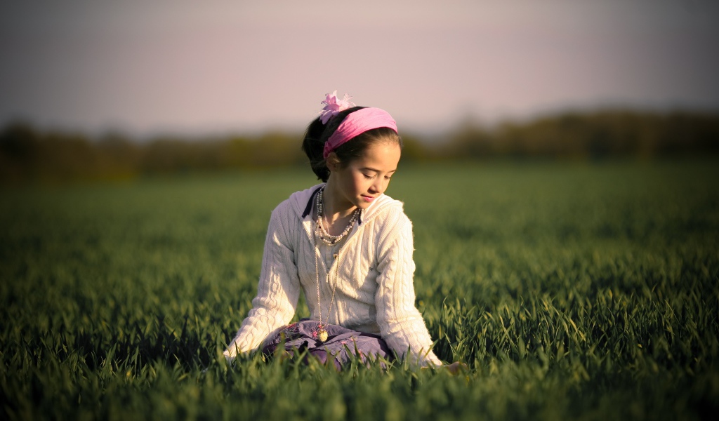 Девочка с розовой повязкой на голове сидит в зеленой траве