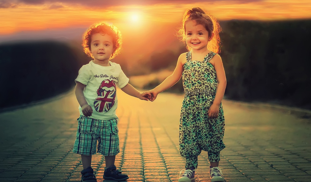 Счастливые мальчик и девочка на дороге на фоне заката