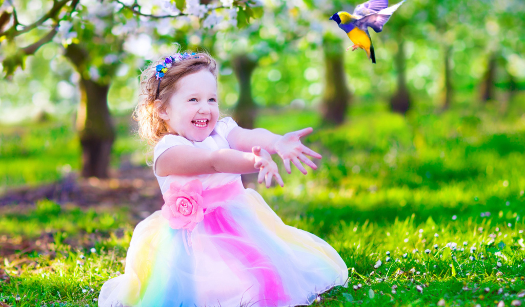 Смеющаяся маленькая девочка в красивом платье на зеленой траве