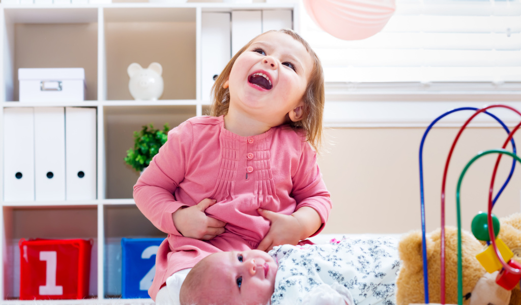 Смеющаяся маленькая девочка с младенцем