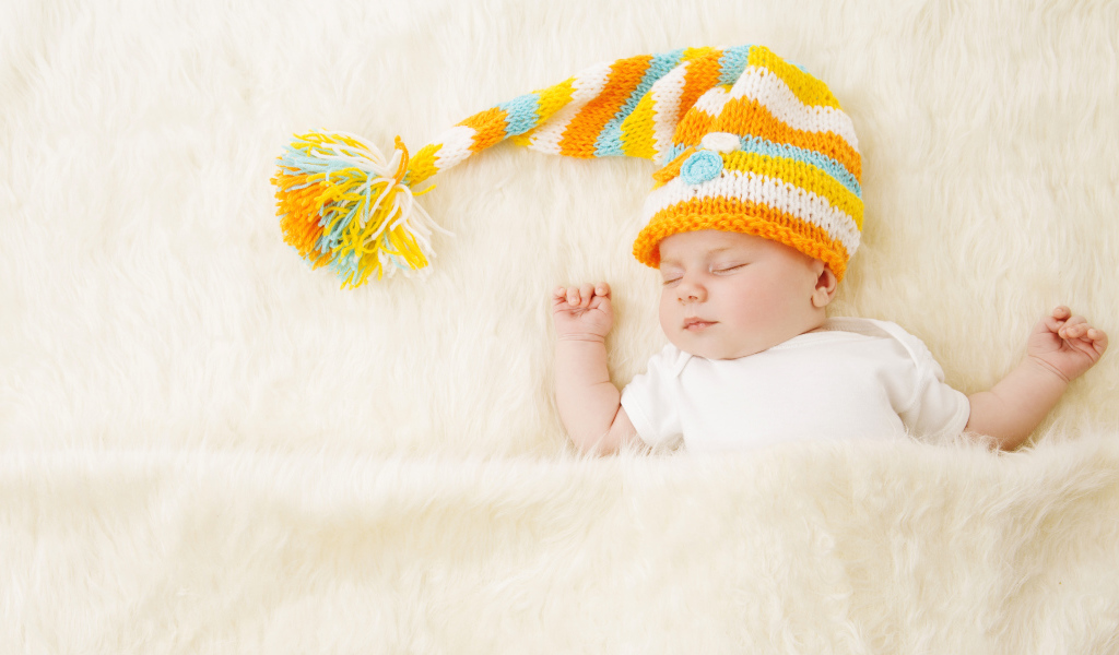 Маленький спящий под меховым покрывалом малыш в вязаной шапке