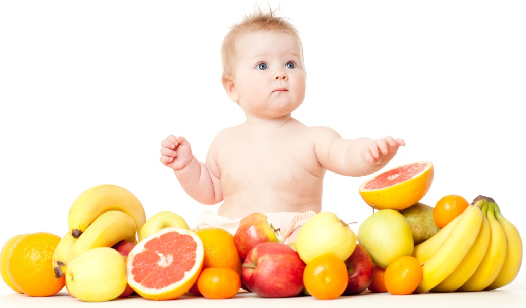 Маленький голубоглазый ребенок с фруктами на белом фоне