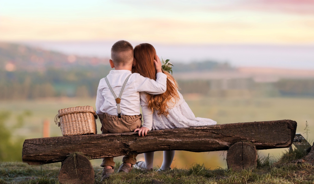 Маленькие мальчик и девочка обнимают друг друга на лавке