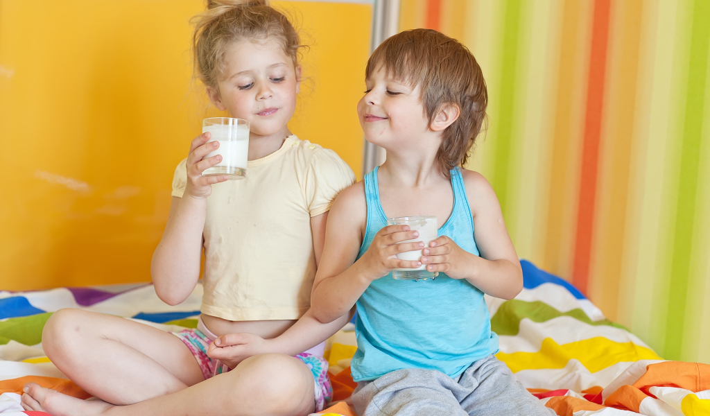 Маленькие мальчик и девочка со стаканами молока в руках 