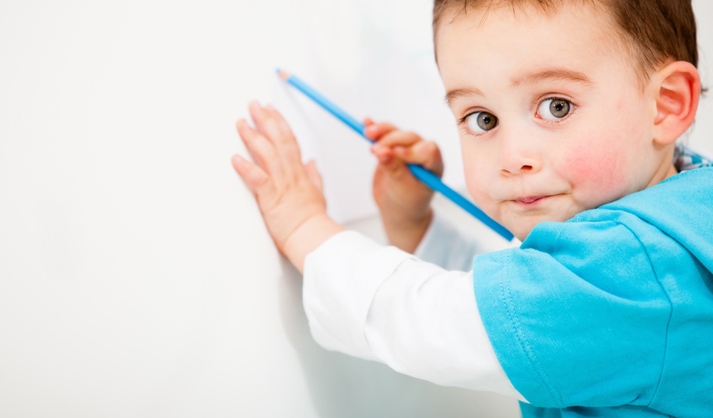 Маленький мальчик рисует карандашом на стене