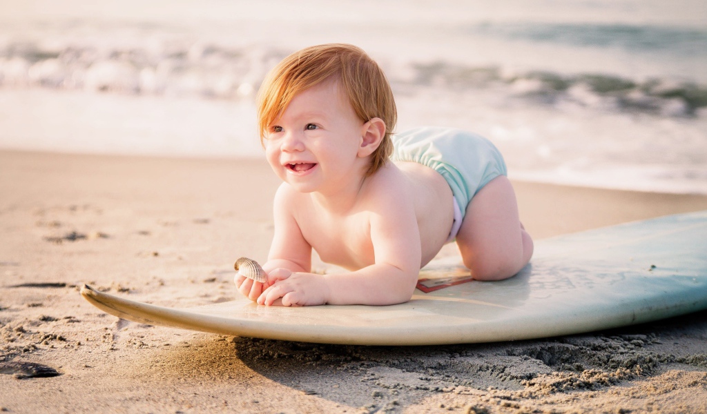 Маленький мальчик на доске для серфинга на пляже