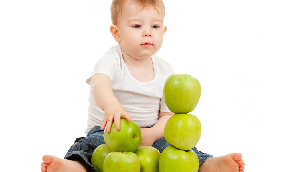 Маленький мальчик играет с зелеными яблоками на белом фоне