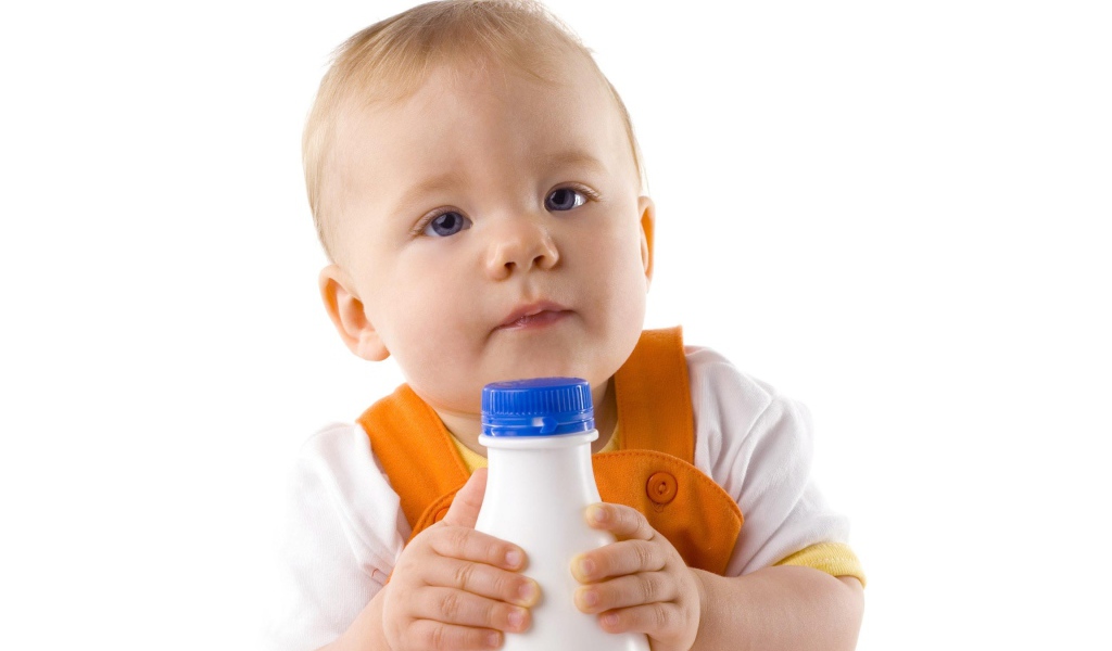 Маленький мальчик с бутылкой молока на белом фоне