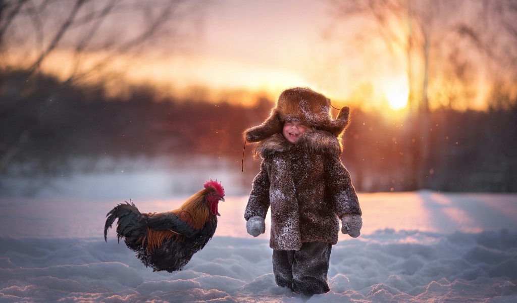 Маленький мальчик с петухом на снегу зимой