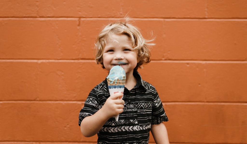 Маленький мальчик с мороженым в руках у стены
