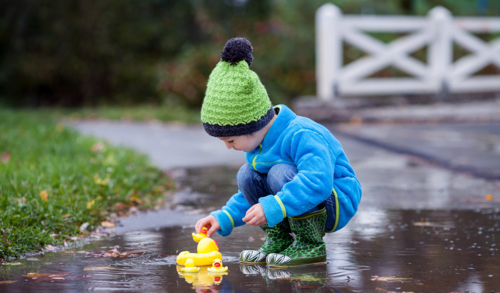 Маленький мальчик с резиновыми уточками в луже осенью