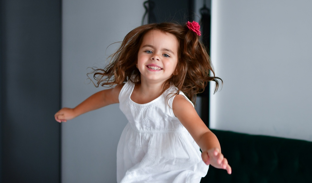 Маленькая веселая девочка в белом платье