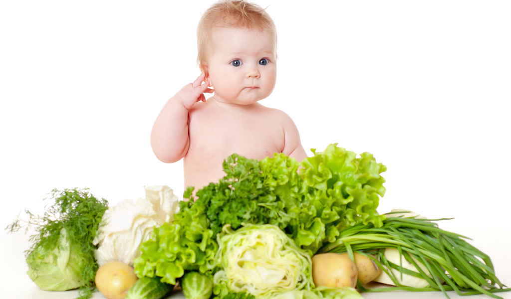 Маленький ребенок с овощами и зеленью на белом фоне