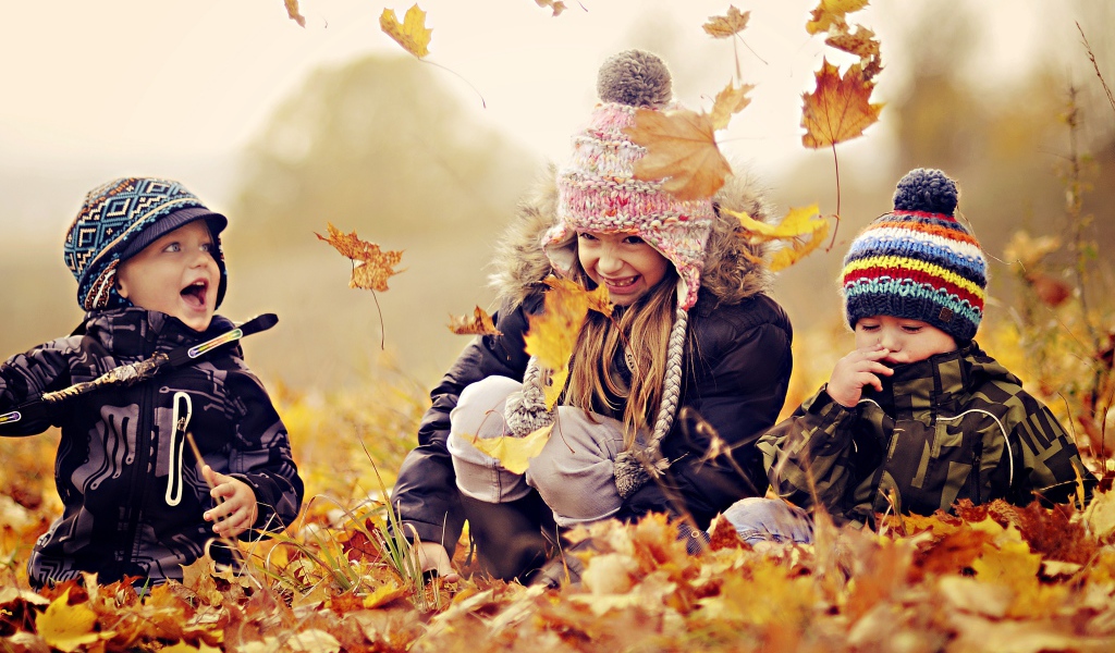 Маленькие дети играют на опавшей желтой листве осенью