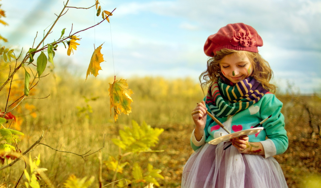 Маленькая девочка рисует красками на листьях осенью 