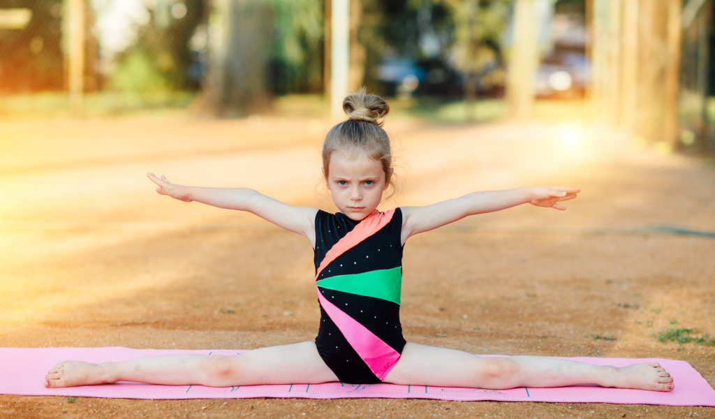 Маленькая девочка гимнастка сидит на шпагате 