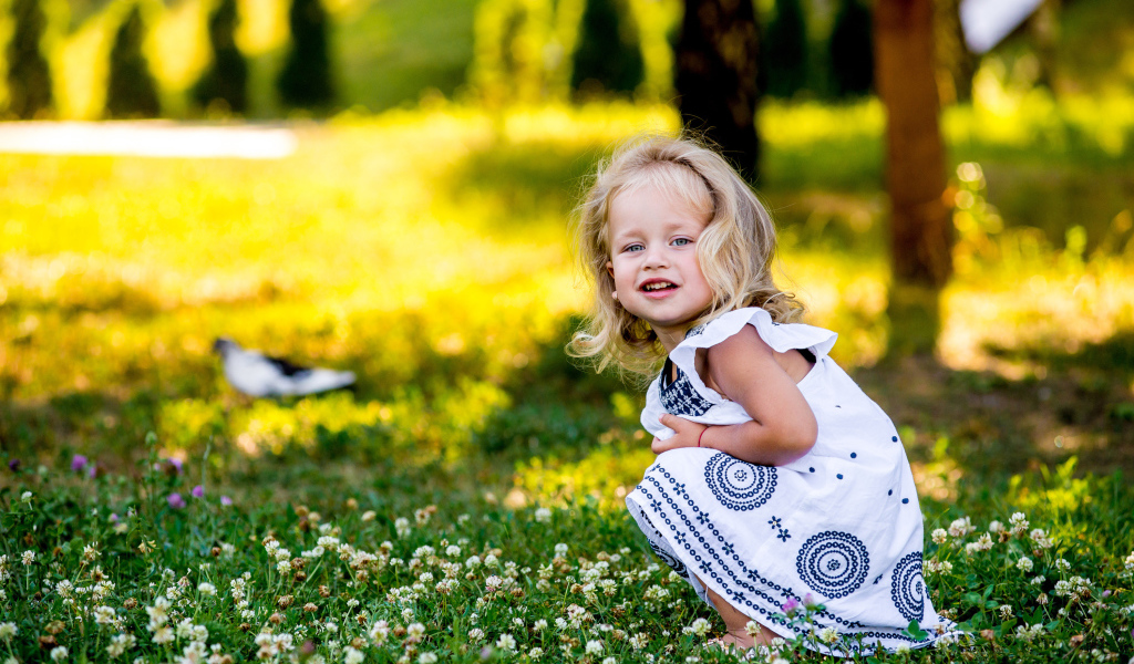 Маленькая девочка в красивом платье сидит на зеленой траве