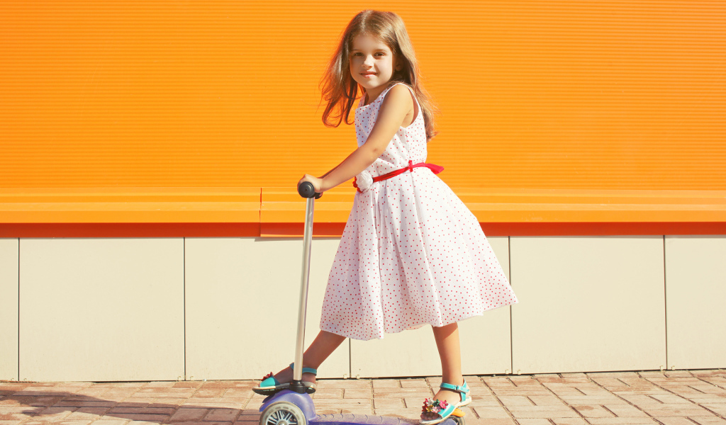 Маленькая девочка в платье на самокате 
