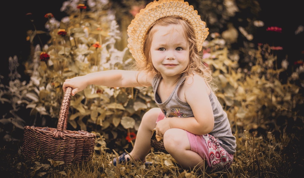 Маленькая девочка в шляпе сидит на траве с корзиной