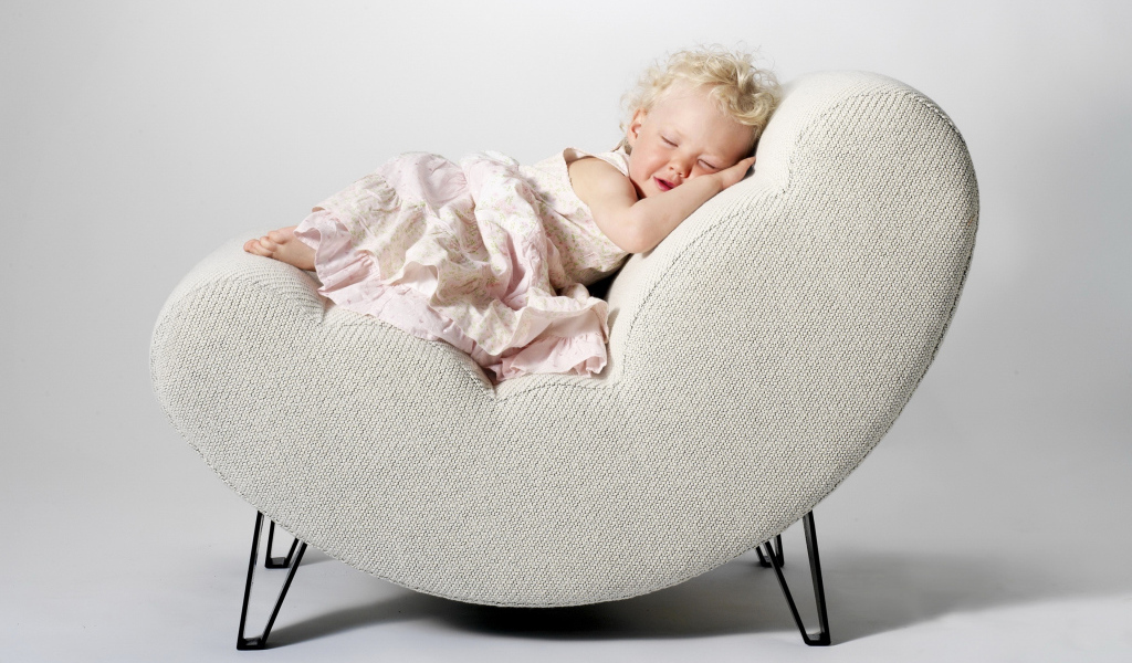 Маленькая девочка в розовом платье спит в кресле