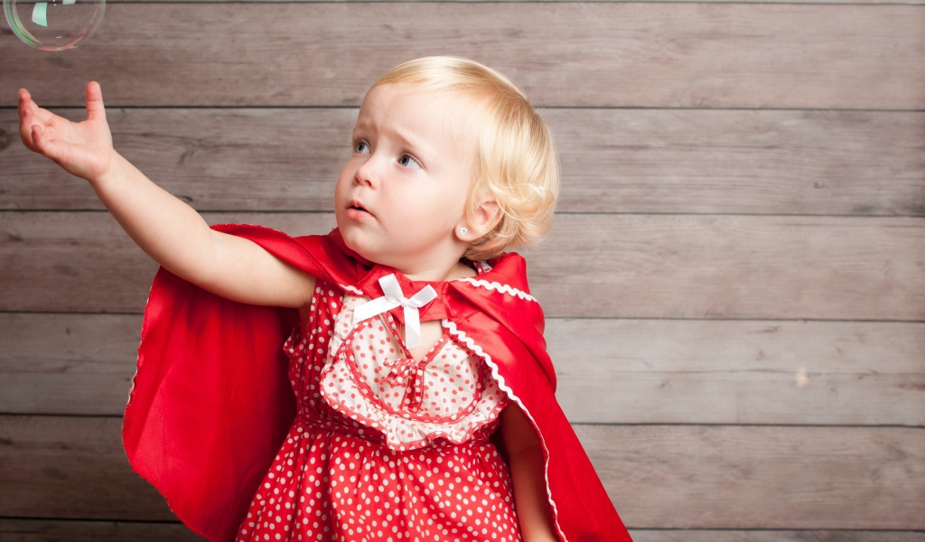 Маленькая девочка в красном платье ловит мыльный пузырь