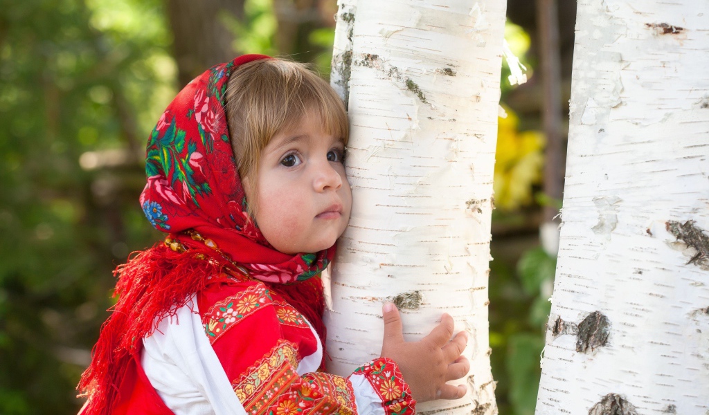 Маленькая девочка в красном платке обнимает березу