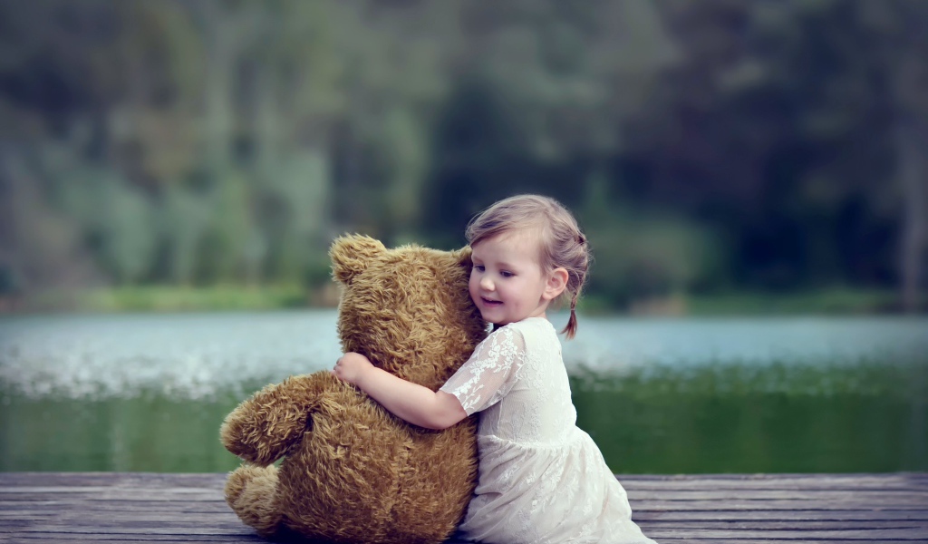 Маленькая девочка в белом платье сидит на мосту с плюшевым медведем