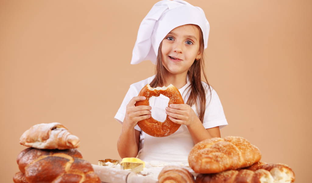 Маленькая девочка в костюме повара и свежей выпечкой