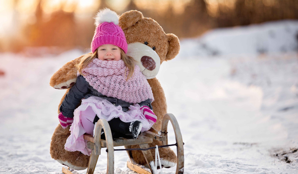 Маленькая девочка на санках с большим медведем зимой 