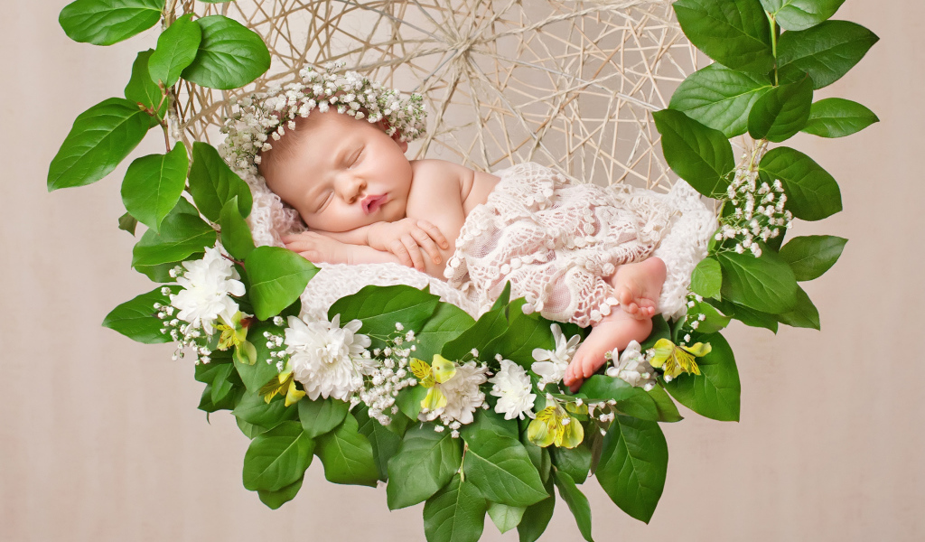 Маленькая девочка спит в колыбеле украшенной зелеными листьями