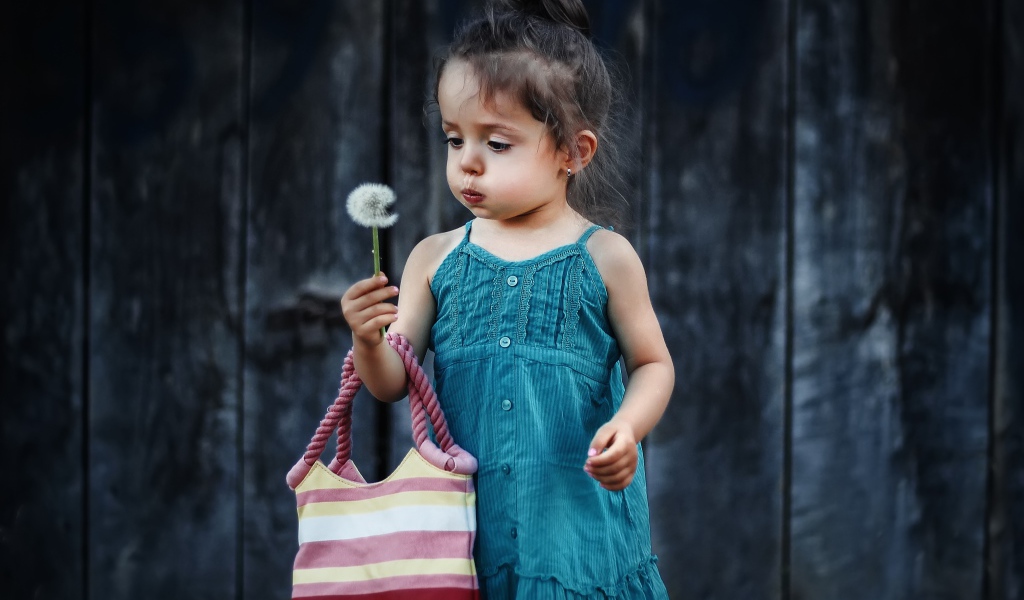 Маленькая девочка с сумкой и одуванчиком в руке